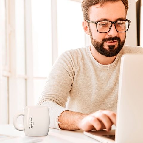 Mitarbeiter im Büro sitzt am Laptop mit einer Tasse Tee