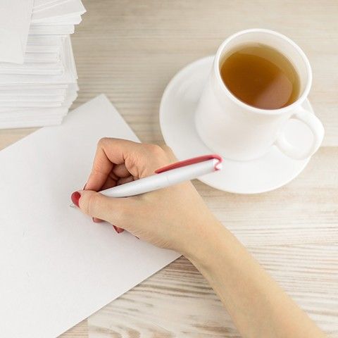 Eine Dame schreibt mit einem Stift auf einem Blatt und einer Tasse Tee
