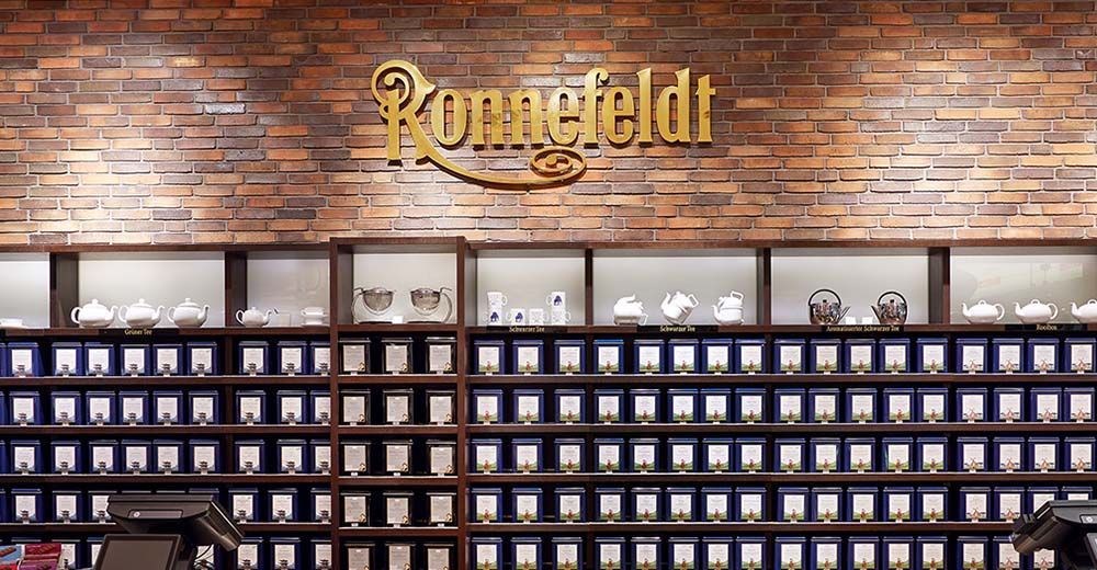 Ronnefeldt Brandstore Frankfurt mit Regalwand voller eleganter Teedosen und goldfarbenem Ronnefeldt-Logo auf Backsteinwand