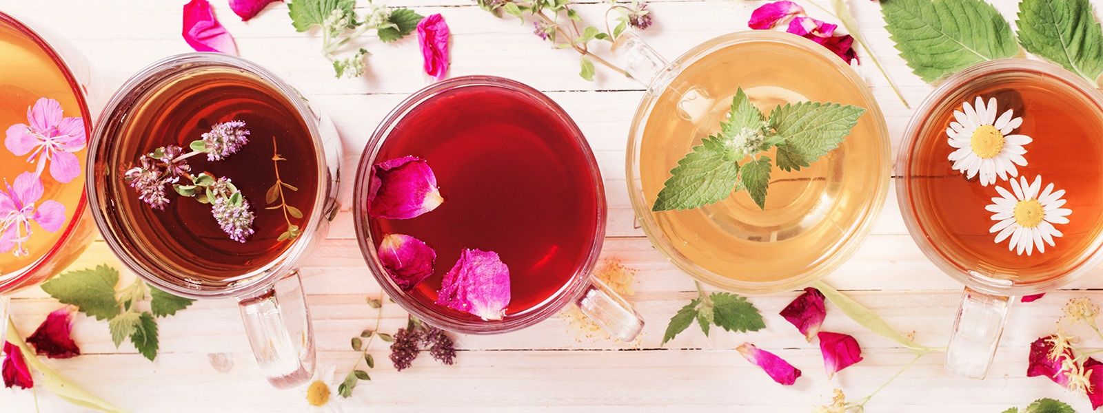 Verschiedenfarbige Tees mit Blütendeko von oben