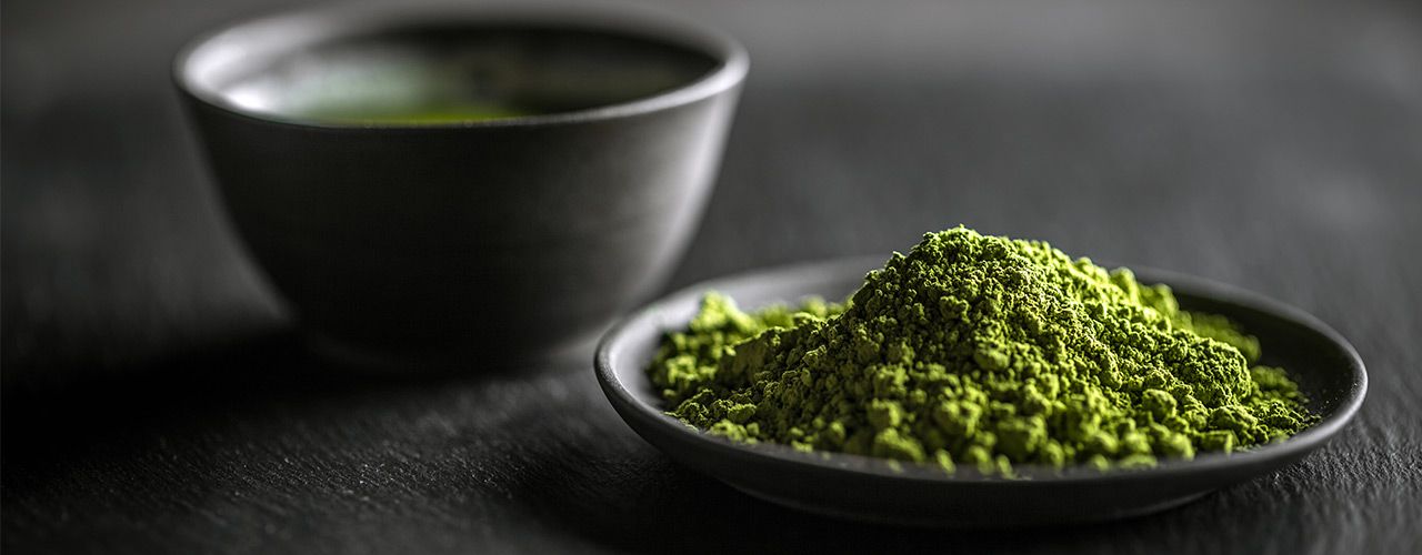 Matchapulver in einer schwarzen Schale, dahinter Schale mit Matcha-Tee