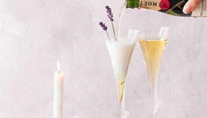 Zwei mit Sekt gefüllte Gläser, eines dekoriert mit Lavendel, daneben eine brennende Kerze