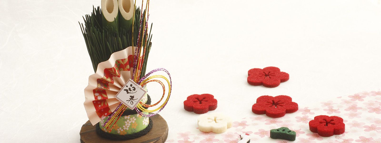 Japanische Neujahrsdekoration mit Kadomatsu aus Bambus und Kiefernzweigen, umgeben von roten und weißen Filzblüten