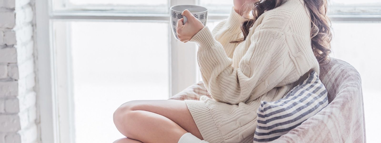 Frau in Wollklamotten auf einem Sessel mit einer Teetasse in der Hand