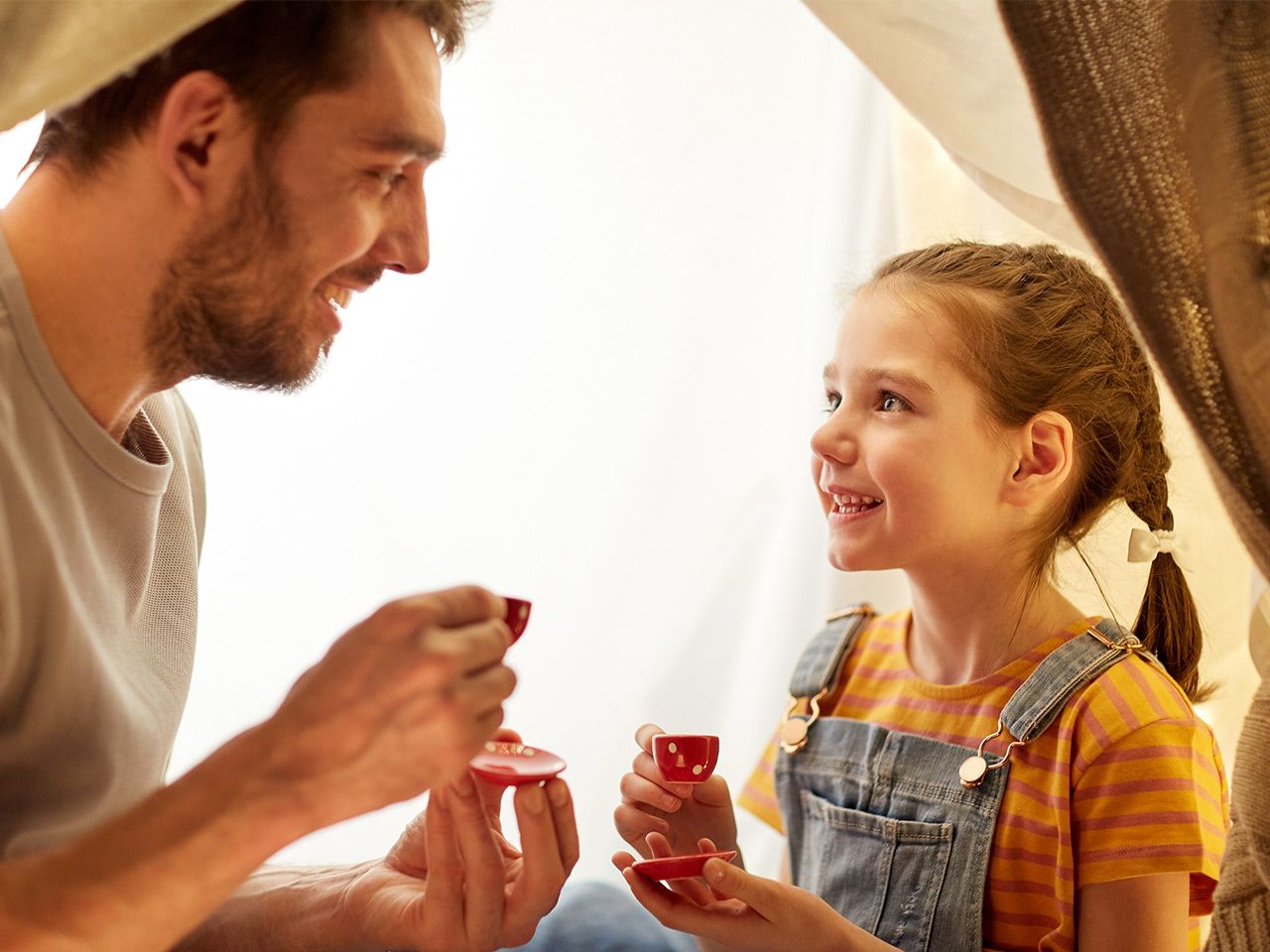 Vster und Tochter trinken lachend Tee aus kleinen Tassen