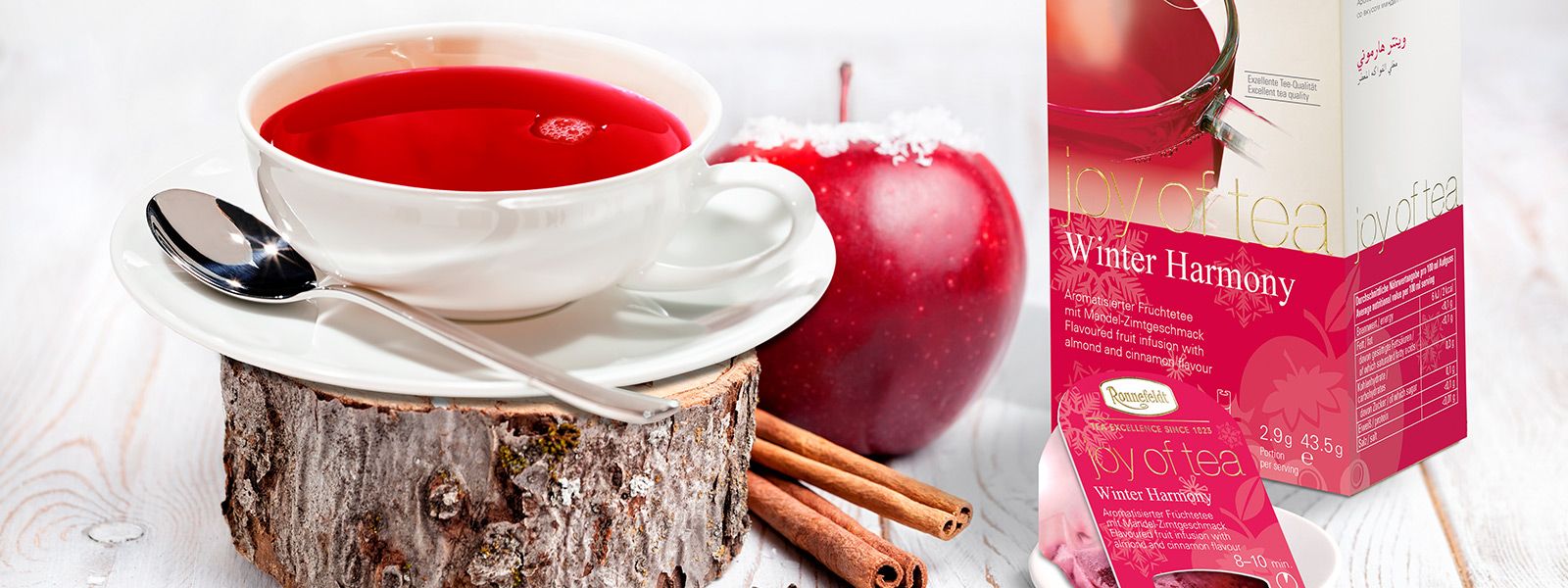 Tasse Tee auf einem Baumstamm im Hintergrund ein Apfel und eine Teeverpackung