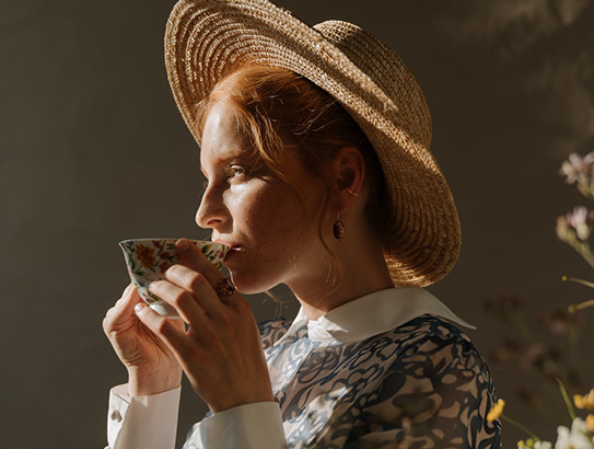 Frau mit Hut trinkt aus Teetasse
